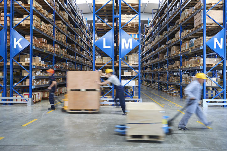 Wearhouse workers tow large trolleys through a lofty warehouse