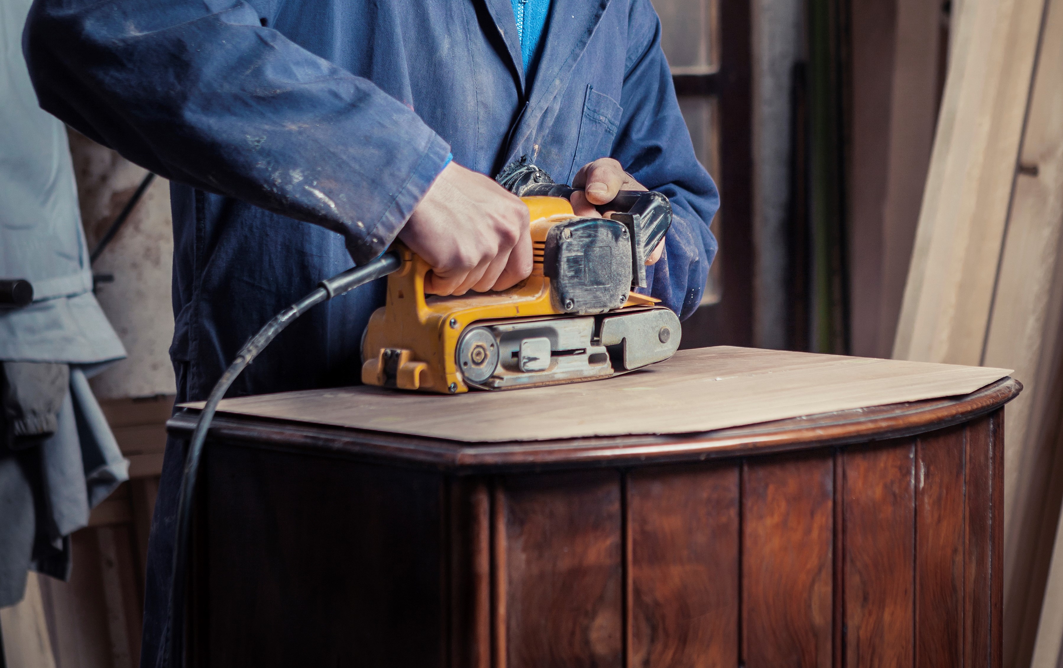 Woodworker sands the top of a wooden cabinet of 